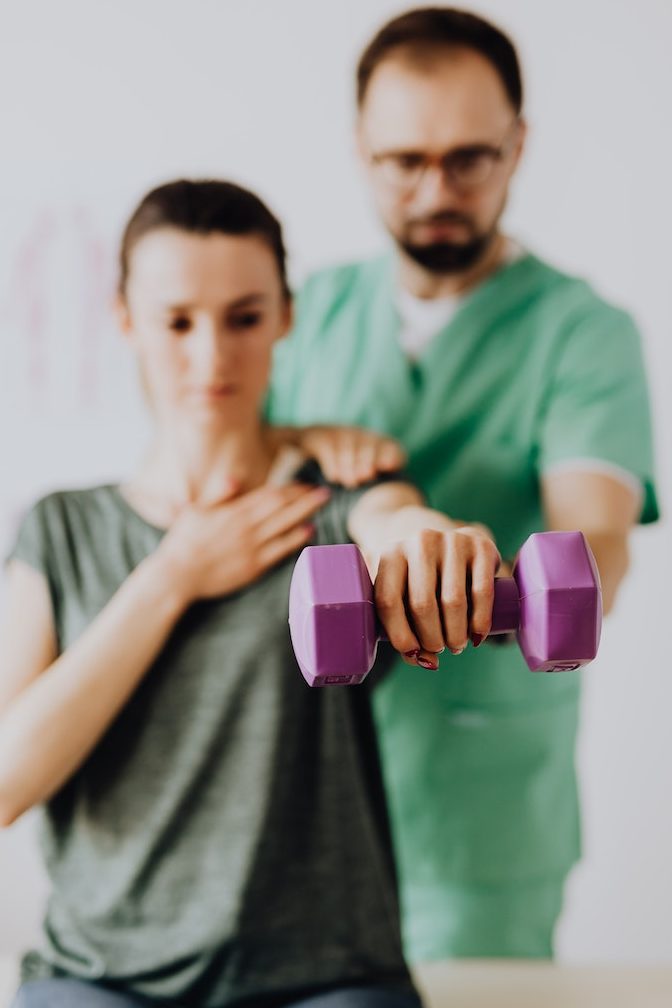 Chiropractor assisting female patient with dumbbell in doctor office